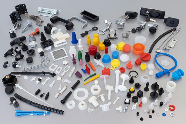 A variety of colorful plastic and metal mechanical parts are arranged on a light gray surface, including handles, caps, and fasteners.